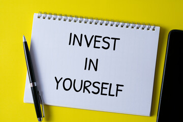 Selective focus of pen and notebook written with INVEST IN YOURSELF on yellow background.