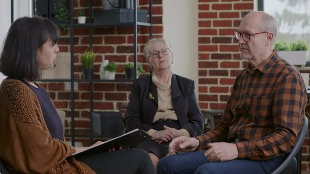 Senior person having discussion with woman about alcohol addiction at aa meeting. Man sharing story about progress and recovery with people in circle at rehabilitation program.