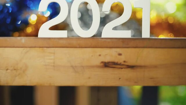 white text number 2021 on a wooden table and change into 2022 by hand with colorful blurred boken background and natural light in the morning. close-up and Tilt up camera shots, New Year change concep