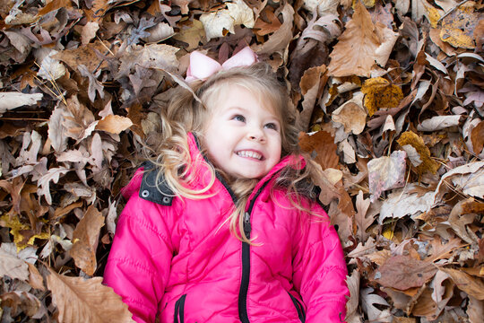 Happy child in the park. Smiling little girl in the leaves. Enjoying warm autumn. 