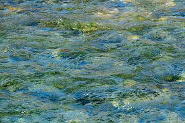 Fototapeta na wymiar Close up view of a flowing creek with pristine clear water running over colorful rocks.