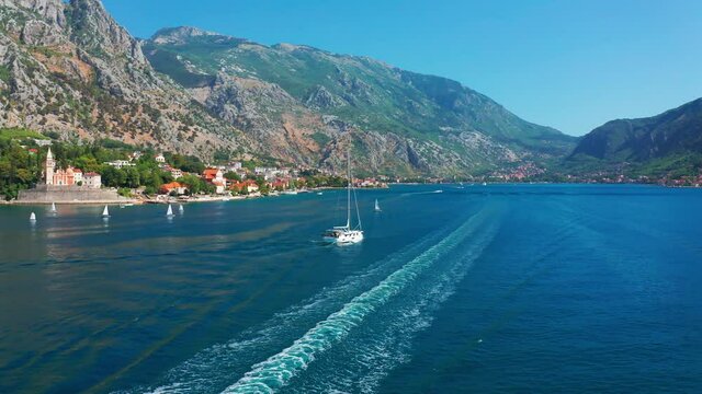Boka Bay with a sailing yacht and boats for water cruises. Beautiful summer landscape of the Bay of Kotor coastline. Aerial drone view 4K.