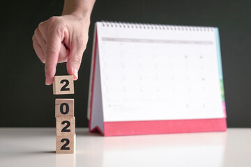 Hand on 2022 wood cubes with calendar at the background. New year, new start. Copy space.