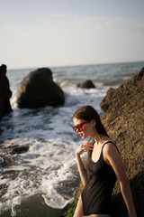 woman in swimsuit sunglasses ocean rocks posing