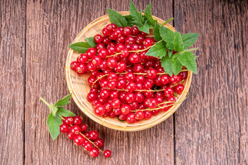 Red currant in bamboo basket on wooden background, Red currant berries with leaf on wooden table.