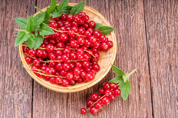 Red currant in bamboo basket on wooden background, Red currant berries with leaf on wooden table.