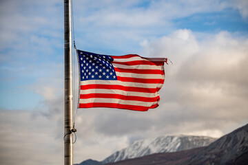 United States of America flag flying half mast with blue sky, clouds and mountain background in the north during fall, autumn season. 
