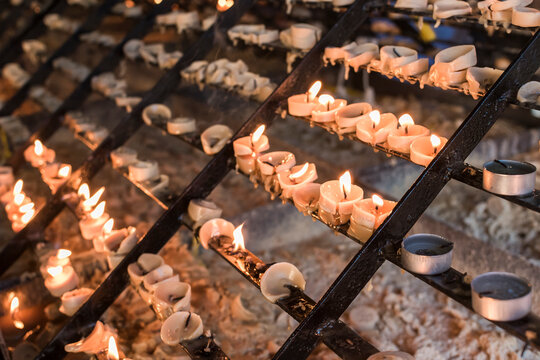 Lit and melted prayer candles placed on a candle rack. Shot at Baclaran church, Philippines.