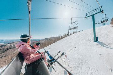 Ski holidays - Woman skier using phone in ski lift. Ski winter vacation concept. Skiing on snow...