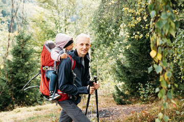 Fototapeta na wymiar Sleepy tired child walking with father in backpack in the mountains. Nordic walk with family and kid in fall. obstacles and challenges for man traveling outdoors. Adventure hiking tour 