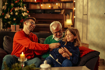 Grandfather and father tickling little boy at home
