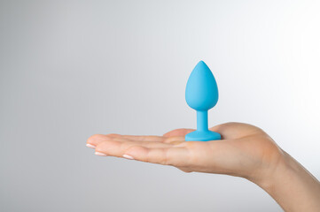 Woman holding a blue anal plug on a white background. Adult toy for alternative sex