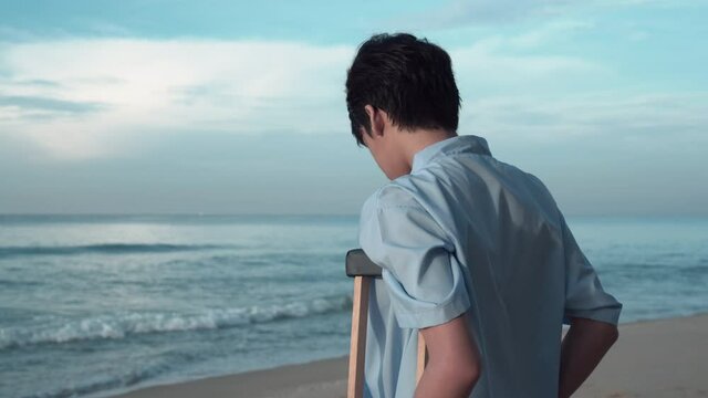 Young patients with crutches relaxing on beach, Disabled man with crutches while travel on the beach.