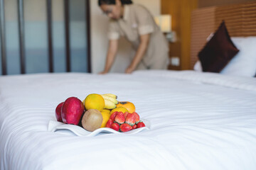 Focus on fruit. A hotel room cleaning maid with fruit put the tray to the bed to welcome the...