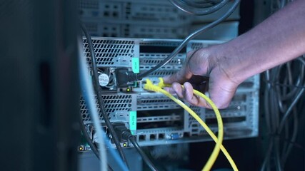 Engineer IT technician sets up system. African-American man switches colorful cables spbas to run checkup of server equipment on rack in data center closeup