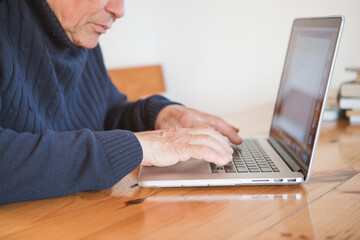 Old hands on the keyboard. Retired person  learn to use computer. Old man working on laptop at home. Senior man using computer in living room, sitting on chair and looking at screen. Elderly grandfath