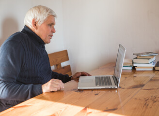 Smiling senior man  wave to camera having video call on laptop, happy elderly male  sit  at home talk using modern technologies and wireless connection