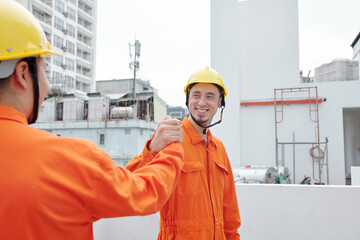Cheerful construction worker shaking hand of his colleague after they finished work on the roof