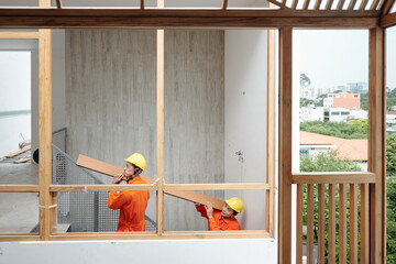 Team of construction workers carrying thick heavy board to the second floor where they are laying...