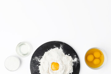 Raw egg yolk in pile of flour on white background