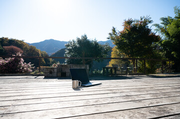 リモートワークなどに使いやすいウッドデッキにパソコンとコーヒーを置いたイメージ