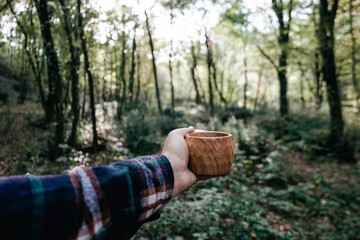 A man holds a traditional wooden Kuksa mug. Autumn forest, close-up.