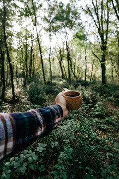 A man holds a traditional wooden Kuksa mug. Autumn forest, close-up. © sercansamanci