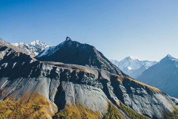 Scenic alpine landscape with sharp rocky pinnacle and snow-covered mountain in sunlight in autumn....