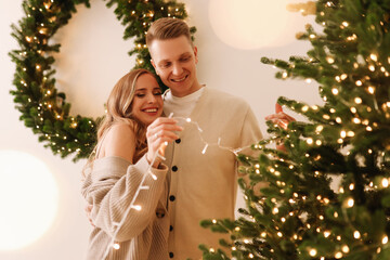 A married couple in love are preparing together for the Christmas holiday during the New Year holidays in a decorated house. Two people decorate the Christmas tree in anticipation of the holiday. 