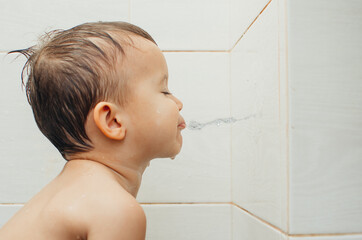 A child sitting in the bathroom spits water on the wall