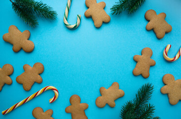 Christmas gingerbread cookies in the shape of man with lollipops and fir branches on blue background, copyspace