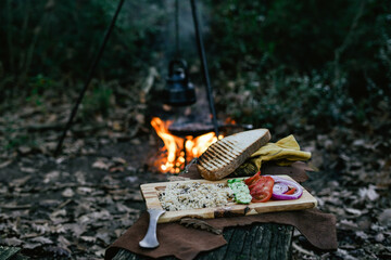 Campfire spool and salad in pan, water bottle and titanium mug near the fire outdoors. bushcraft, adventure, travel, tourism and camping concept