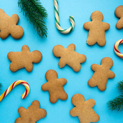 Christmas gingerbread cookies in the shape of man with lollipops and fir branches on blue background, top view