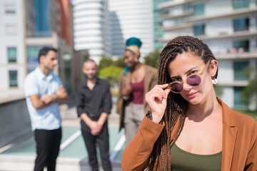 Attractive caucasian woman on terrace roof party. Long-haired female in casual clothes and sunglasses. People of different nationalities standing in background. Teambuilding, party concept