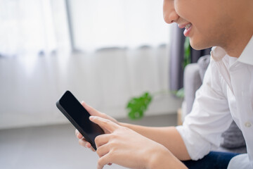 Happy smiling young man using modern smartphone device while sitting on sofa at home.