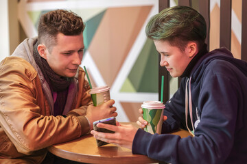 A guy and a girl are sitting in a cafe and using smartphones. Communication, technology, internet.