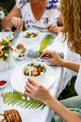 Family celebrations and food concept. The family is having dinner at a summer garden party. Table setting and decoration. Food and drinks. BBQ, vegetables, wine and other snacks. Life in the suburbs