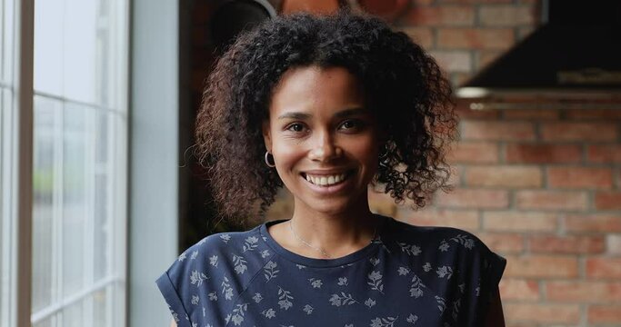 Head shot of attractive African woman standing in kitchen pose look at camera. 30s millennial female having natural afro curly hair and wide toothy smile, natural beauty, happy person portrait concept