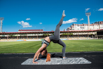 Fototapeta na wymiar Fit woman doing stretching on mat at outdoor in sity stadium