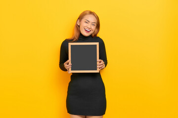 Fototapeta premium Smiling young Asian woman holding chalkboard isolated over yellow background