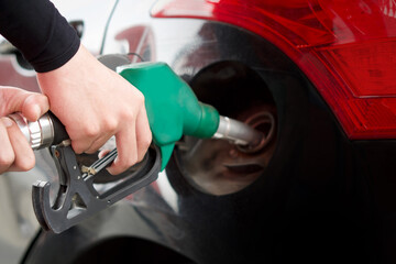 Closeup hand holding green  gas pump nozzle. Gas station worker filling up black car.