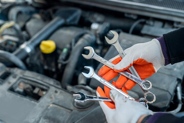 man's hand in a special glove holds tools for a car near the car