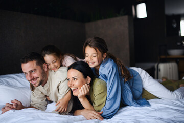 Happy young family with two children lying on bed at hotel, summer holiday.