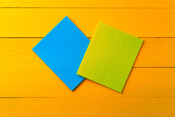Colored cleaning rags on yellow wooden background