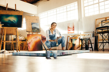 Cheerful young artist squatting close to her painting - obrazy, fototapety, plakaty