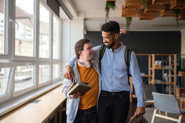 Young man with Down syndrome and his tutor with arms around looking at each other indoors at school - obrazy, fototapety, plakaty