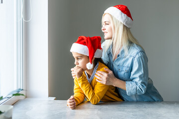 Obraz premium Adorable caucasian blond mom with daughter both wearing Santa caps