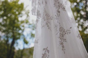 Wedding dress hanging on tree on background of wooden structure among summer greenery