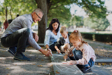 Senior couple with grandchildren drawing with chalks on pavement outdoors in park.