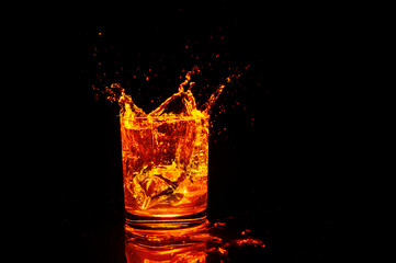 glass with brown liquid with ice cubes and bottom illumination on dark background